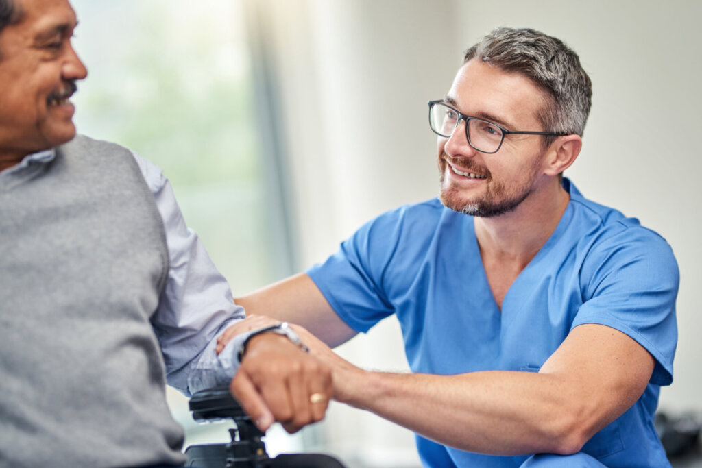 Male nurse smiling and patting the arm of a memory care resident at Traditions at Lakeview Crossing in Groveport, OH.