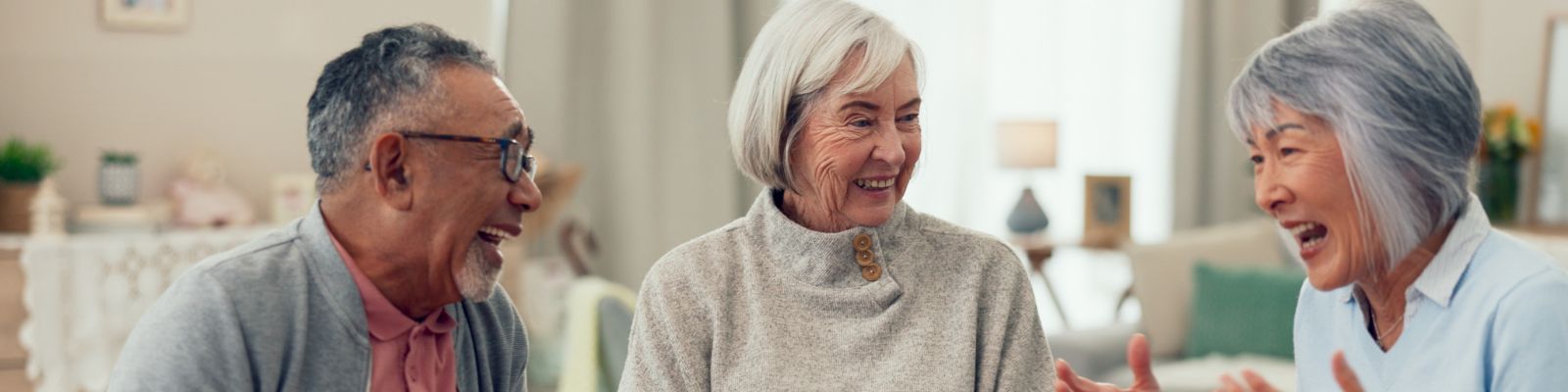 three senior adults sitting together indoors, facing each other as they have a joyful, animated conversation