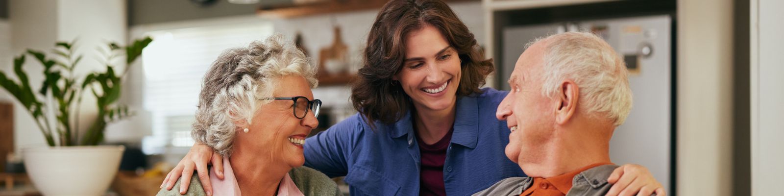 a smiling younger woman with her arms affectionately around the shoulders of an older man and an older woman